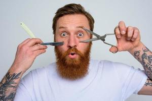 Wondered man with scissors and blade is ready to cut the beard photo