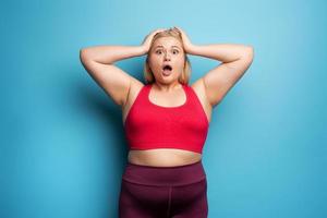 Fat girl is worried because the scale marks a high weight. Cyan background photo