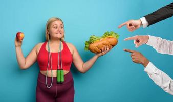 Fat girl is undecided to eat an apple or a big sandwich. cyan background photo