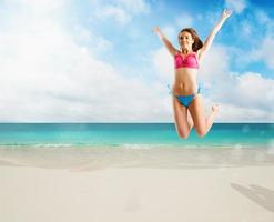 mujer en bikini traje de baño saltando desde alegría en tropical playa foto