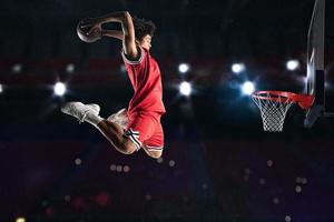 Basketball player in red uniform jumping high to make a slam dunk to the basket photo