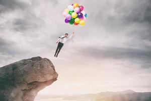 Creative businessman holding colorful balloons flies from the peak of a mountain photo