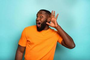 Man speaks in the ear to a friend about a great promotion. amazed expression. cyan background photo