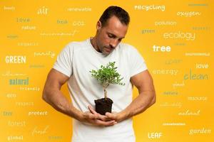 Boy cradles a small tree ready to be planted. yellow color background. concept of forestation, ecology and conservation with most important terms photo