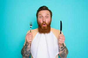 Shocked man with tattoos is ready to eat something with cutlery in hand photo