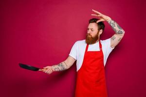 serious chef with beard and red apron cooks with pan photo