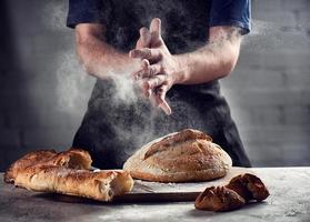 Chef sprinkles fresh bread with flour in the kitchen photo