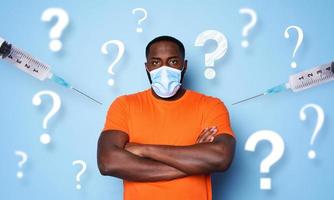 Man with face mask has a lot of questions and doubts about covid 19 vaccine. cyan background photo