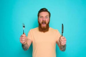 Hungry man with tattoos is ready to eat with cutlery in hand photo