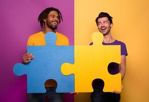 Friends with puzzles in hand over yellow background. Concept of integration, union and partnership photo