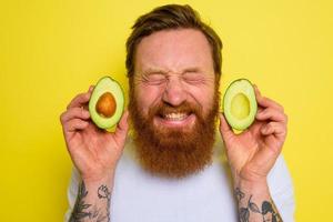 Happy man with beard and tattoos holds an avocado photo