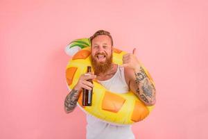 contento hombre es Listo a nadar con un rosquilla salvador de la vida con cerveza y cigarrillo en mano foto