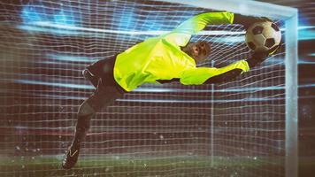 fútbol portero, en fluorescente uniforme, hace un salvar y evita un objetivo durante un noche partido foto