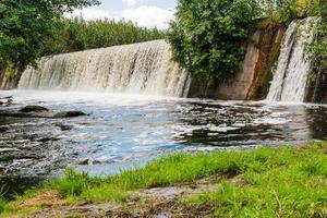 Waterfall on a background of green grass and blue sky photo