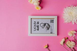 White photo frame with flowers on pink background