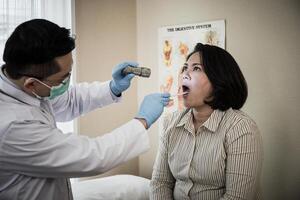 médico en blanco uniforme vestido chequeo del paciente boca con Linterna foto