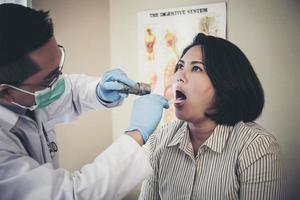médico en blanco uniforme vestido chequeo del paciente boca con Linterna foto
