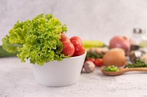 photo lettuce and tomatoes in a white cup with sliced onions and fresh peppers on the cement floor.