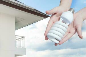 Energy saving concept, Woman hand holding light bulb on house background,Ideas light bulb in the hand photo