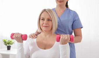 A physiotherapist helps an older woman recover from an injury through exercise with dumbbells. photo