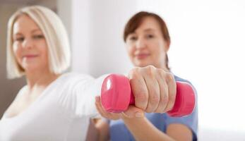 A physiotherapist helps an older woman recover from an injury through exercise with dumbbells. photo