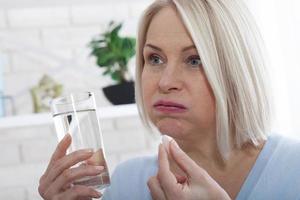 Woman hold glass still water and pill. Sick woman taking putting pill in mouth painkiller or antibiotic medicine, depression treatment chronic disease or biologically active supplement concept photo