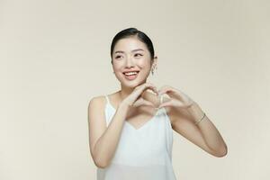 Portrait of positive young lady with healthy smooth skin holding hands in the shape of a heart near face photo