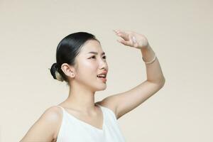 Young asian woman raising hand to covering her face from sunlight against a beige background photo