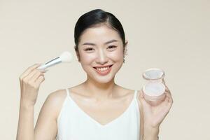 Portrait of beautiful young woman looking at the mirror putting on makeup holding a makeup brush photo