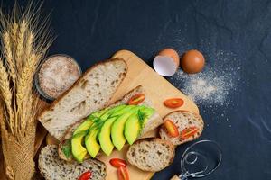 sliced avocado with dill leaves on baguette bread on black background, photo