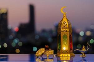 linterna que tiene el símbolo de la luna en la parte superior y un pequeño plato de dátiles con cielo nocturno y fondo claro de la ciudad para la fiesta musulmana del mes sagrado del ramadán kareem. foto