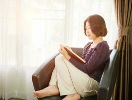 joven mujer asiática de pelo corto lee un libro en la sala de estar foto