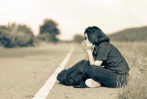 Woman sit with backpack hitchhiking along a road in countryside photo