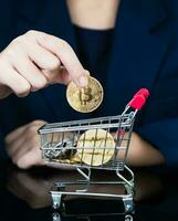 Woman holding some pieces of golden Bitcoin token in shopping cart photo