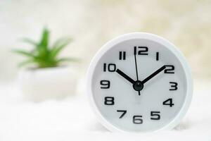 White alarm clock and little decorative tree in vase on table photo