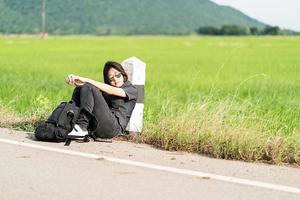 Woman sit with backpack hitchhiking along a road photo