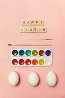 Inscription HAPPY EASTER letters eggs colorful paints isolated on trendy pastel pink background photo