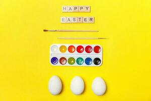 Inscription HAPPY EASTER letters eggs colorful paints isolated on trendy yellow background photo