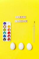 Inscription HAPPY EASTER letters eggs colorful paints isolated on trendy yellow background photo