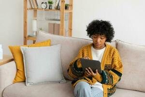 African american girl holding digital tablet touch screen typing scroll page at home. Woman with mobile tech device surfing internet using social media apps playing game. Study work shopping online. photo