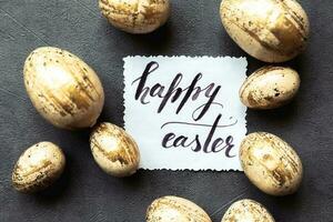 Happy Easter concept. Preparation for holiday. Golden Easter eggs Inscription HAPPY EASTER letters text on grunge scratched dark black shale background. Flat lay top view copy space. photo