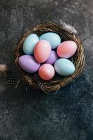Happy Easter concept. Preparation for holiday. Colorful pastel decorated easter eggs in nest on grunge scratched dark black shale background. Simple minimalism flat lay top view copy space. photo