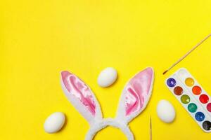 Decorative eggs colorful paints and bunny ears furry costume toy isolated on trendy yellow background photo