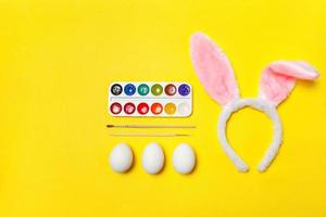 Decorative eggs colorful paints and bunny ears furry costume toy isolated on trendy yellow background photo