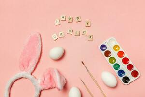 Inscription HAPPY EASTER letters eggs colorful paints and bunny ears isolated on trendy pink background photo