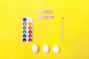Inscription HAPPY EASTER letters eggs colorful paints isolated on trendy yellow background photo