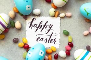 Happy Easter concept. Preparation for holiday. Easter eggs Inscription HAPPY EASTER letters candy chocolate eggs and jellybean sweets on concrete stone grey background. Flat lay top view copy space. photo