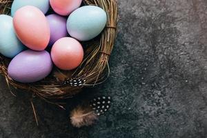 Happy Easter concept. Preparation for holiday. Colorful pastel decorated easter eggs in nest on grunge scratched dark black shale background. Simple minimalism flat lay top view copy space. photo