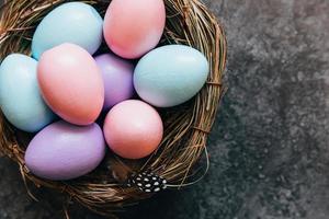 Happy Easter concept. Preparation for holiday. Colorful pastel decorated easter eggs in nest on grunge scratched dark black shale background. Simple minimalism flat lay top view copy space. photo