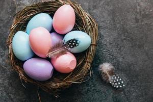 Happy Easter concept. Preparation for holiday. Colorful pastel decorated easter eggs in nest on grunge scratched dark black shale background. Simple minimalism flat lay top view copy space. photo